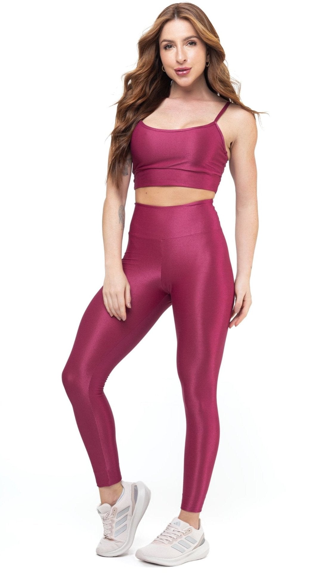 Woman in magenta workout set—crop top with thin straps and high-waisted leggings—paired with pink sneakers. Ideal for gym or casual wear.