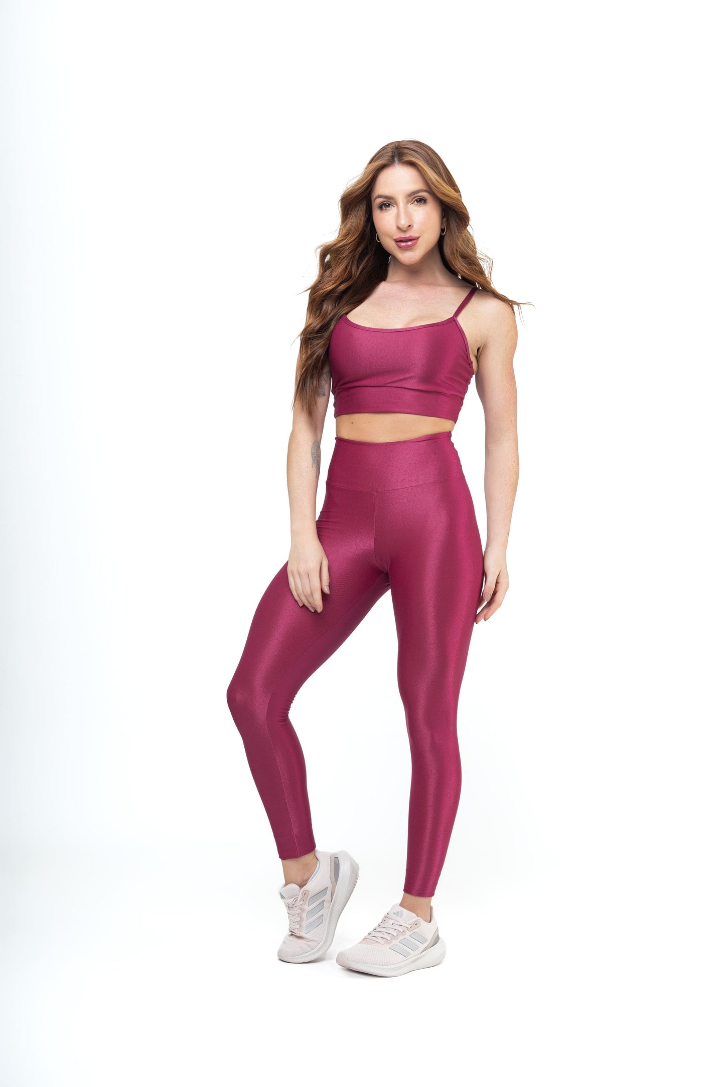 Woman in magenta workout set—crop top with thin straps and high-waisted leggings—paired with pink sneakers. Ideal for gym or casual wear.